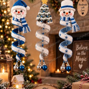 May include: Three hanging crochet ornaments featuring a snowman in a blue hat, a Christmas tree with a yellow star, and a snowman in a white hat. Each ornament has a long, spiralling tail decorated with blue and white patterns and small bells.