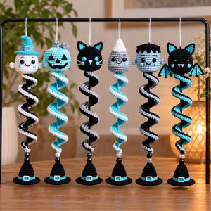 May include: Six hanging crochet ornaments featuring Halloween characters including a ghost, pumpkin, cat, ghost, monster, and bat. Each figure sits atop a long, spiralling tail in black, white, and turquoise, ending with a small black witch hat base.