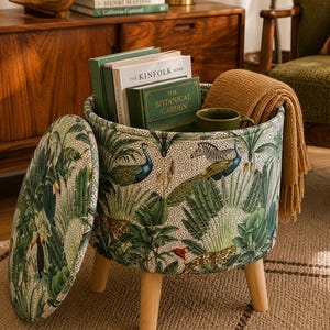 May include: A round storage ottoman with a jungle-themed fabric featuring peacocks, toucans, and leopards. The lid is open, revealing books, a mug, and a blanket. The ottoman has wooden legs.