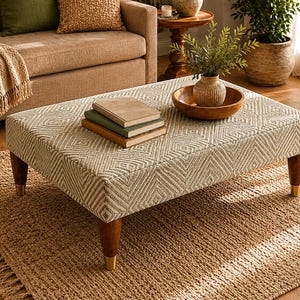 Könnte beinhalten: Ein rechteckiger Hocker mit einem geometrischen Muster in Beige- und Cremetönen. Er hat dunkle Holzbeine mit goldfarbenen Spitzen. Der Hocker befindet sich in einem Wohnzimmer, mit Büchern, einer Holzschale und einer Vase mit Grünzeug.