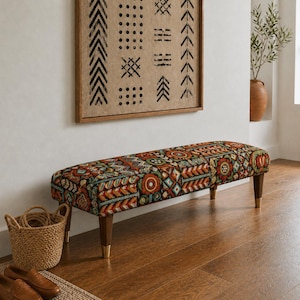 Puede incluir: Un banco estampado con un diseño colorido con detalles en rojo, naranja, verde azulado y dorado. El banco tiene patas de madera con puntas doradas. Una cesta tejida se encuentra a la izquierda del banco.