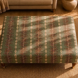 Puede incluir: Un otomán rectangular tapizado en tela de color verde salvia con un patrón vertical repetitivo de hojas de color marrón oscuro similares a helechos y pequeñas formas de diamante de color crema. Se apoya sobre cuatro patas de madera cónicas.