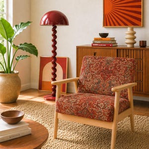 Puede incluir: Interior de salón con una lámpara de pie roja en espiral y un sillón estampado. Una mesa auxiliar de madera con libros y un cuenco pequeño. La habitación está decorada con una alfombra y obras de arte.