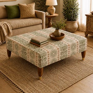 May include: A square ottoman upholstered in a cream-coloured fabric featuring a repeating pattern of sage green circular botanical motifs and vertical orange stripes. The piece is supported by four tapered wooden legs with gold-toned metal feet.