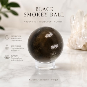 Puede incluir: Una piedra esférica pulida, de color marrón oscuro y translúcido, que descansa sobre un soporte circular transparente. El texto en la imagen dice: BLACK SMOKEY BALL, GROUNDING, PROTECTION, CLARITY, y enumera beneficios para protección, conexión y claridad.