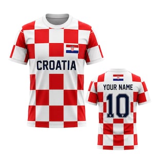 Może przedstawiać: Biało-czerwona koszulka piłkarska Chorwacji w kratkę. Z przodu koszulki napis "CROATIA" w kolorze granatowym oraz chorwacka flaga. Z tyłu napis "YOUR NAME" nad numerem "10" w kolorze granatowym.