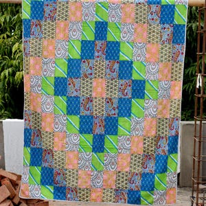 May include: A rectangular patchwork quilt featuring a repeating grid of fabric squares in vibrant shades of lime green, royal blue, soft pink, and intricate paisley patterns in black, white, and red, finished with a thin white piped border.