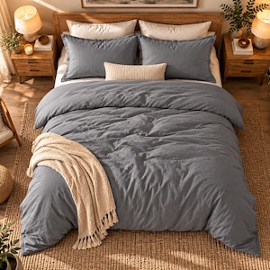 May include: A slate blue duvet cover set featuring two matching pillow shams, a long rectangular cream-coloured lumbar pillow, and a textured cream-coloured throw blanket with fringe draped across the foot of the bed on a wooden bed frame.