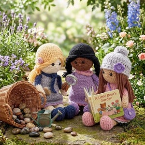 Puede incluir: Tres muñecas de ganchillo con pelo de lana y ropa. Una muñeca tiene pelo rubio y vestido azul, otra tiene pelo negro y vestido morado con una lupa, y otra tiene pelo castaño, un gorro gris y un libro titulado A Little Bear's Garden.