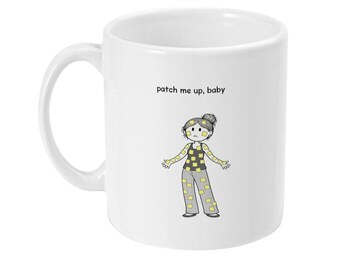 Puede incluir: Taza de cerámica blanca con una ilustración de dibujos animados de una persona con ropa de retazos. El texto "patch me up, baby" está impreso encima de la ilustración. La taza tiene un asa curva.