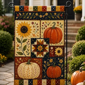 May include: A rectangular garden flag featuring a patchwork design with sunflowers, orange and white pumpkins, and a central star quilt pattern. The border includes small floral motifs in red, yellow, blue, and green on a dark background.