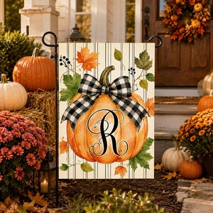 May include: A rectangular garden flag featuring a watercolour illustration of an orange pumpkin with a black and white buffalo check bow. The pumpkin is centred with a large black letter R monogram. The background has thin vertical black stripes.