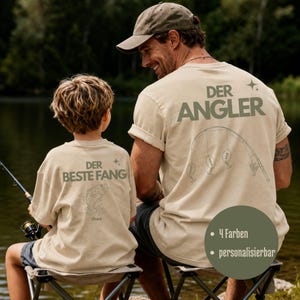 Könnte beinhalten: Zwei beige T-Shirts mit dunkelgrünem Text und Grafiken. Das größere Shirt zeigt den Text DER ANGLER und eine Angelruten-Illustration. Das kleinere Shirt zeigt den Text DER BESTE FANG und eine Fisch-Illustration mit dem Namen theo.