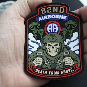 May include: A rectangular rubber patch featuring a skull wearing a green military helmet and gear. The text 82ND AIRBORNE appears at the top, with the AA insignia in the center and the phrase DEATH FROM ABOVE on a red banner at the bottom.