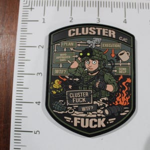 May include: A shield-shaped morale patch featuring a cartoon soldier with night vision goggles, a rubber duck, and a spilled coffee mug. The text reads CLUSTER, CJC, PLAN, EXECUTION, WHO APPROVED THIS, WTF, SEND HELP, and CLUSTER FUCK. It measures 3.5 inches tall.