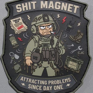 May include: A shield-shaped morale patch in olive green and black featuring a cartoon soldier covered in mud. The text reads SHIT MAGNET and ATTRACTING PROBLEMS SINCE DAY ONE. Surrounding the soldier are icons of a radio, boot, wrench, and documents.