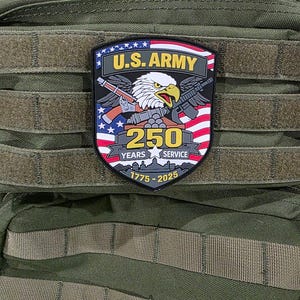 May include: A patch featuring the U.S. Army emblem with an eagle, guns, and the American flag. The patch commemorates 250 years of service from 1775 to 2025. The patch is on a green tactical backpack.