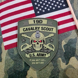 May include: An olive green 19D Cavalry Scout patch with a skull graphic, crossed sabers, and the text "U.S. ARMY." An American flag is in the background. The patch includes the phrase, "If you ain't cav... you ain't shit."