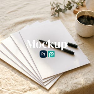 May include: A stack of white paper with the word "Mockup" in a white font. A black pen and pen cap are on top of the paper. The Adobe Photoshop and Adobe Illustrator logos are below the word "Mockup". A cup of coffee is in the background.