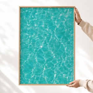 Könnte beinhalten: Ein rechteckiger Wandkunstdruck mit einem lebendigen türkisfarbenen Wasseroberflächenmuster mit weißen Lichtreflexionen und kaustischen Wellen, eingefasst in einen einfachen hellen Holzrahmen mit schlichtem Design.