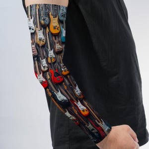 May include: A compression arm sleeve featuring a repeating pattern of electric guitars in various colors including red, yellow, white, blue, and black, set against a dark, weathered wood-grain background, worn on an arm with a black t-shirt.