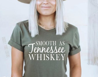 Può includere: Una maglietta verde con la scritta "Smooth as Tennessee Whiskey" stampata in bianco.