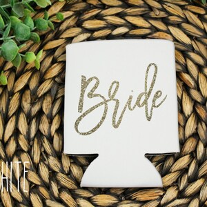 Puede incluir: Enfriador de latas blanco con la palabra "Bride" escrita en letras doradas con purpurina.
