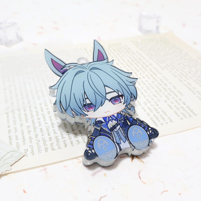 Puede incluir: Un charm de acr&iacute;lico transparente con un personaje de anime chibi con cabello azul claro y ojos morados. El personaje viste un atuendo azul y blanco. El charm tiene un peque&ntilde;o lazo para sujetar. Aproximadamente 7 cm de altura.