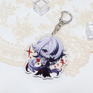 May include: A clear acrylic keychain featuring a chibi anime character with white and black hair, purple eyes, and a black outfit. The keychain has a silver metal ring and clasp. Red star accents are around the character.