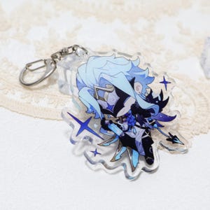 May include: A clear acrylic keychain featuring a cartoon character with light blue hair and a black and white outfit. The keychain has a silver clasp and is decorated with blue star shapes.