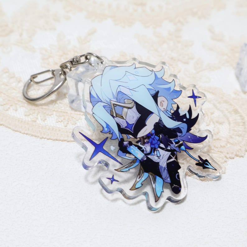 May include: A clear acrylic keychain featuring a cartoon character with light blue hair and a black and white outfit. The keychain has a silver clasp and is decorated with blue star shapes.