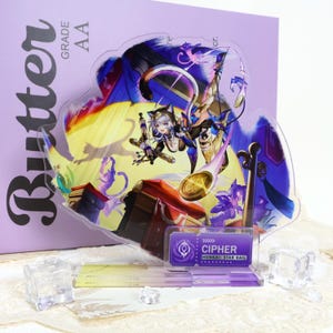Puede incluir: Un expositor de acrílico transparente con un personaje de Honkai Star Rail llamado Cipher, representado en una pose dinámica con un pergamino y una moneda de oro. La base es morada con el texto CIPHER HONKAI STAR RAIL. El fondo es una caja morada con el texto BUTTER GRADE AA.