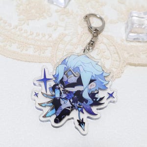 May include: A clear acrylic keychain featuring a stylized anime character with light blue hair and accents. The character has a detailed outfit with dark blue and black elements. The keychain includes a silver clasp and several star-shaped embellishments.