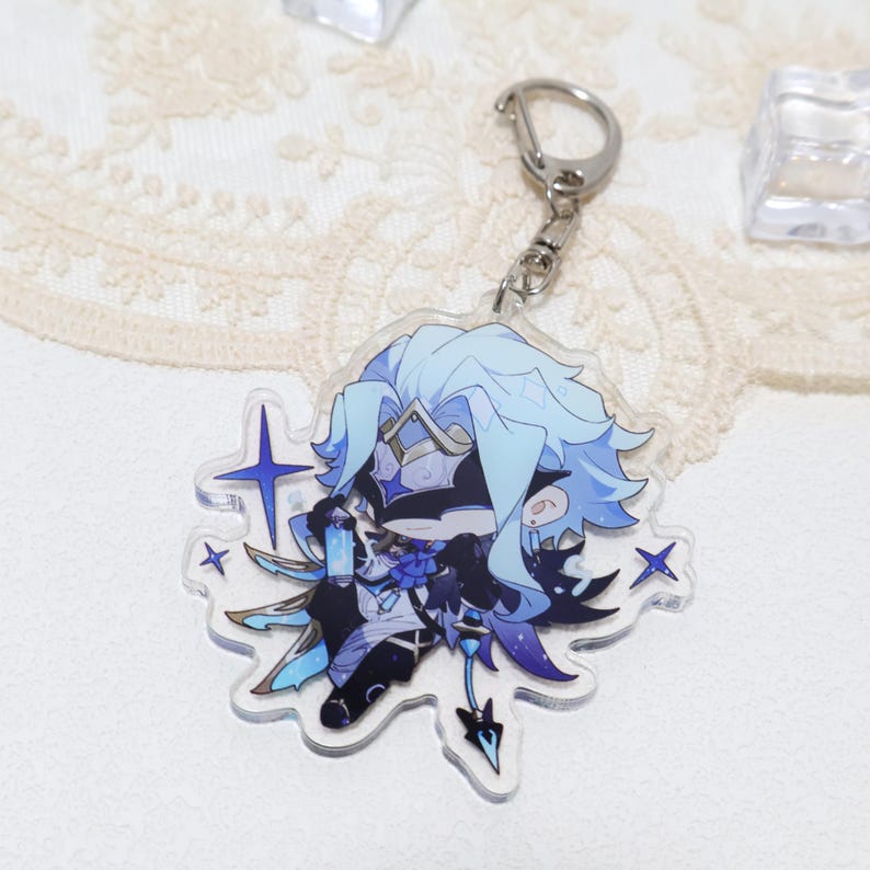 May include: A clear acrylic keychain featuring a stylized anime character with light blue hair and accents. The character has a detailed outfit with dark blue and black elements. The keychain includes a silver clasp and several star-shaped embellishments.