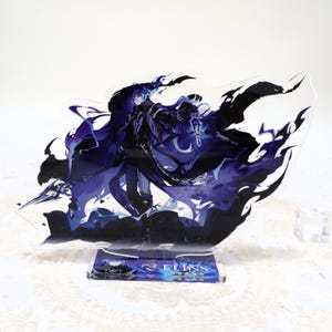 May include: A clear acrylic stand with a detailed illustration of a character with long blue hair and dark clothing, surrounded by swirling black and purple accents. The stand has a rectangular base with the text "FLINS".