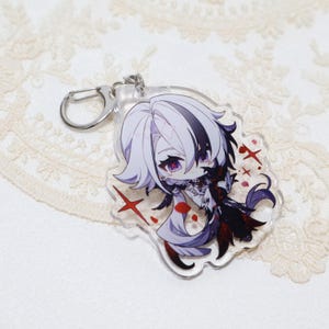May include: A clear acrylic keychain featuring a chibi anime character with white and black hair, red eyes, and a black and red outfit. The keychain has a silver clasp.