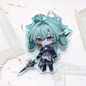 May include: A clear acrylic keyring featuring a chibi anime character with teal hair and purple eyes. The character is dressed in a dark blue and black outfit and holds a spear. The keyring has a silver ring attached.