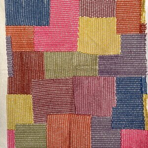 May include: A rectangular textile piece featuring a patchwork design of various colored squares. The fabric displays a grid of stitched blocks in shades of blue, pink, yellow, orange, purple, olive green, and deep red, all joined with visible thread.