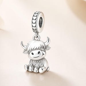Pode incluir: Um berloque de prata com um design de vaca das Highlands. O berloque tem uma apar&ecirc;ncia detalhada e texturizada com um rosto sorridente, chifres e p&ecirc;lo lanoso. A parte superior do berloque tem um anel com recortes em forma de cora&ccedil;&atilde;o.