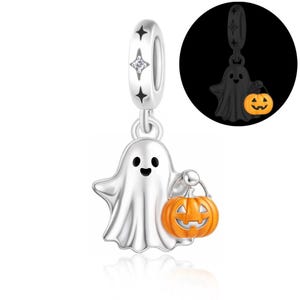 Può includere: Un ciondolo in argento a forma di fantasma che tiene in mano una zucca arancione. Il passante è decorato con motivi a stella neri e una piccola pietra trasparente. Un riquadro mostra la figura del fantasma che brilla al buio.