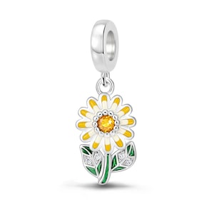 May include: A silver charm featuring a daisy flower with white and yellow enamel petals, a central orange crystal, and a green stem with two leaves accented by small clear stones. The charm has a cylindrical bail for attachment to a bracelet.