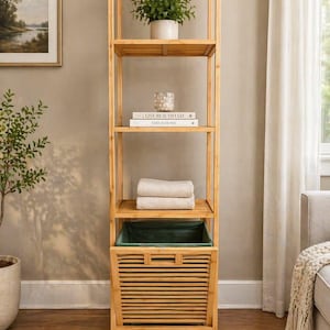 May include: A tall, natural wood shelf unit with four shelves. The top shelf holds a potted plant. Other shelves display books, towels, and a green fabric basket. The unit is in a well-lit room with a neutral color palette.