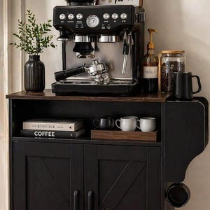 May include: A black espresso machine with a coffee bean container and a sign that says "Rise & Shine It's Coffee Time" sits on a black cabinet. The cabinet has a wooden top and a lower cabinet with two doors.