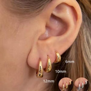 Può includere: Orecchini a cerchio color oro in tre misure: 6 mm, 10 mm e 12 mm. Gli orecchini sono mostrati su un orecchio, con le misure indicate. I cerchi hanno una finitura liscia e lucida e un design classico.