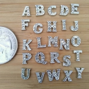 May include: Silver alphabet letter charms with rhinestones. Each letter is individually set on a silver base and has clear rhinestones around the edges. The letters are arranged in alphabetical order from A to Z.