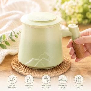 Könnte beinhalten: Hellgrüne Keramik-Tasse mit Deckel, Holzgriff und -fuß. Die Tasse hat ein Bergdesign und steht auf einem gewebten Untersetzer. Der Text lautet: "Natürliche Materialien", "Bleifreie Glasur", "Perfekt für den täglichen Gebrauch", "Minimalistisches Design".