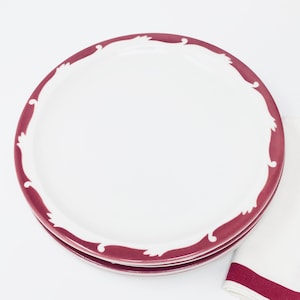 Op de afbeelding: Een set van drie witte keramische dinerborden met een bordeauxrode rand en een decoratief ontwerp.