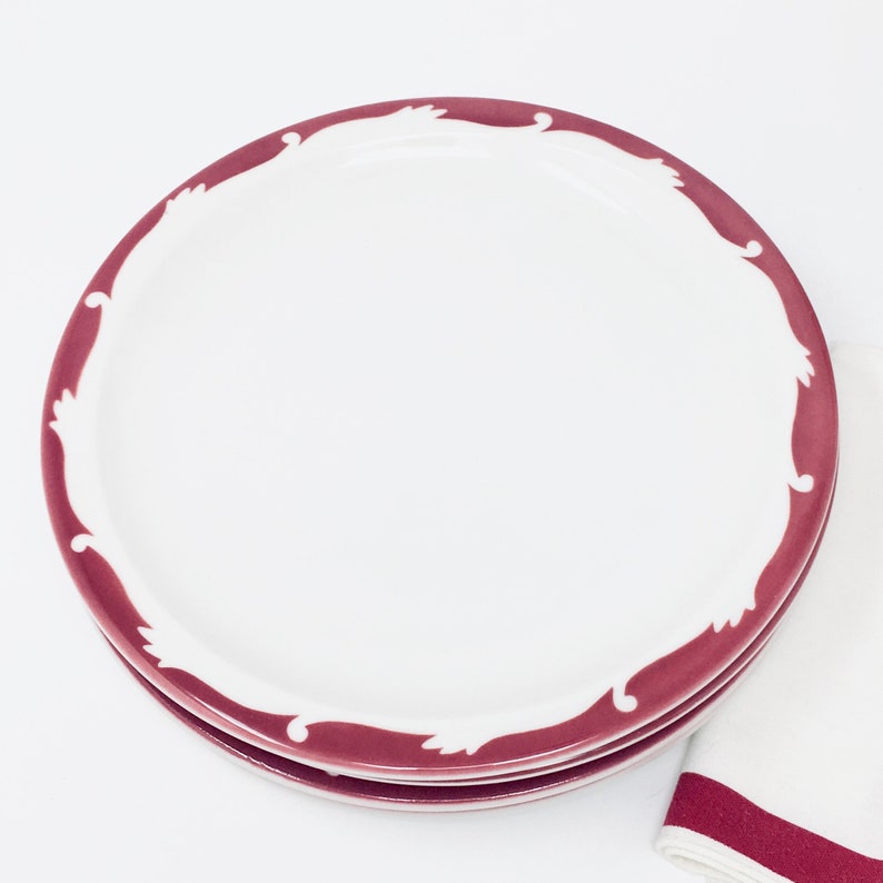 Op de afbeelding: Een set van drie witte keramische dinerborden met een bordeauxrode rand en een decoratief ontwerp.