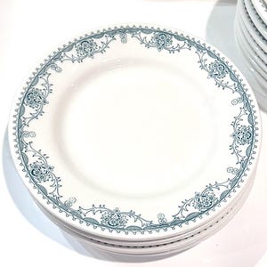 Może przedstawiać: Stos białych ceramicznych talerzy z niebieskim i zielonym wzorem kwiatowym wok&oacute;ł krawędzi.