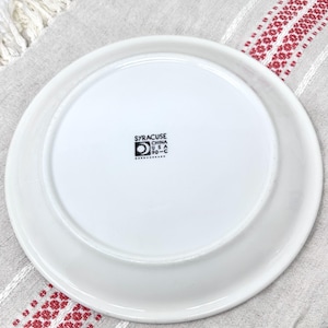 Op de afbeelding: Witte keramische plaat met een zwarte stempel aan de onderkant met de tekst "Syracuse China USA 90-C".